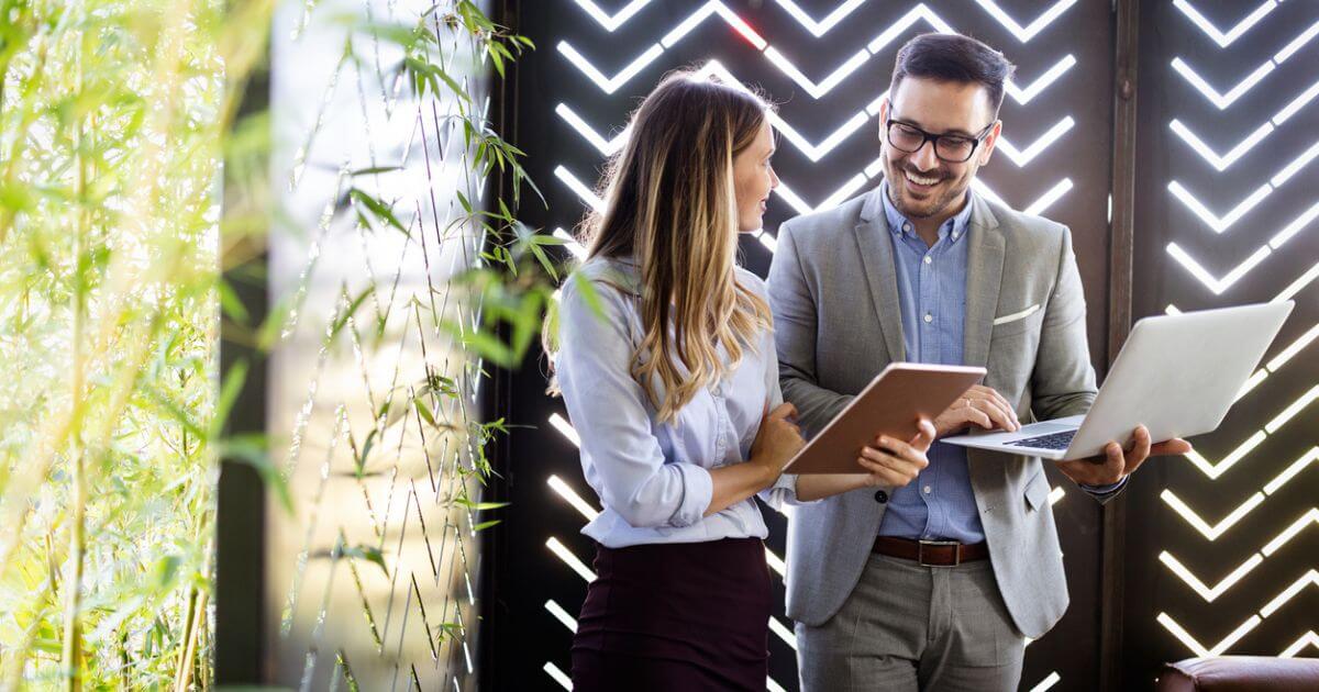 Two people stood in an office with greenery holding their laptops