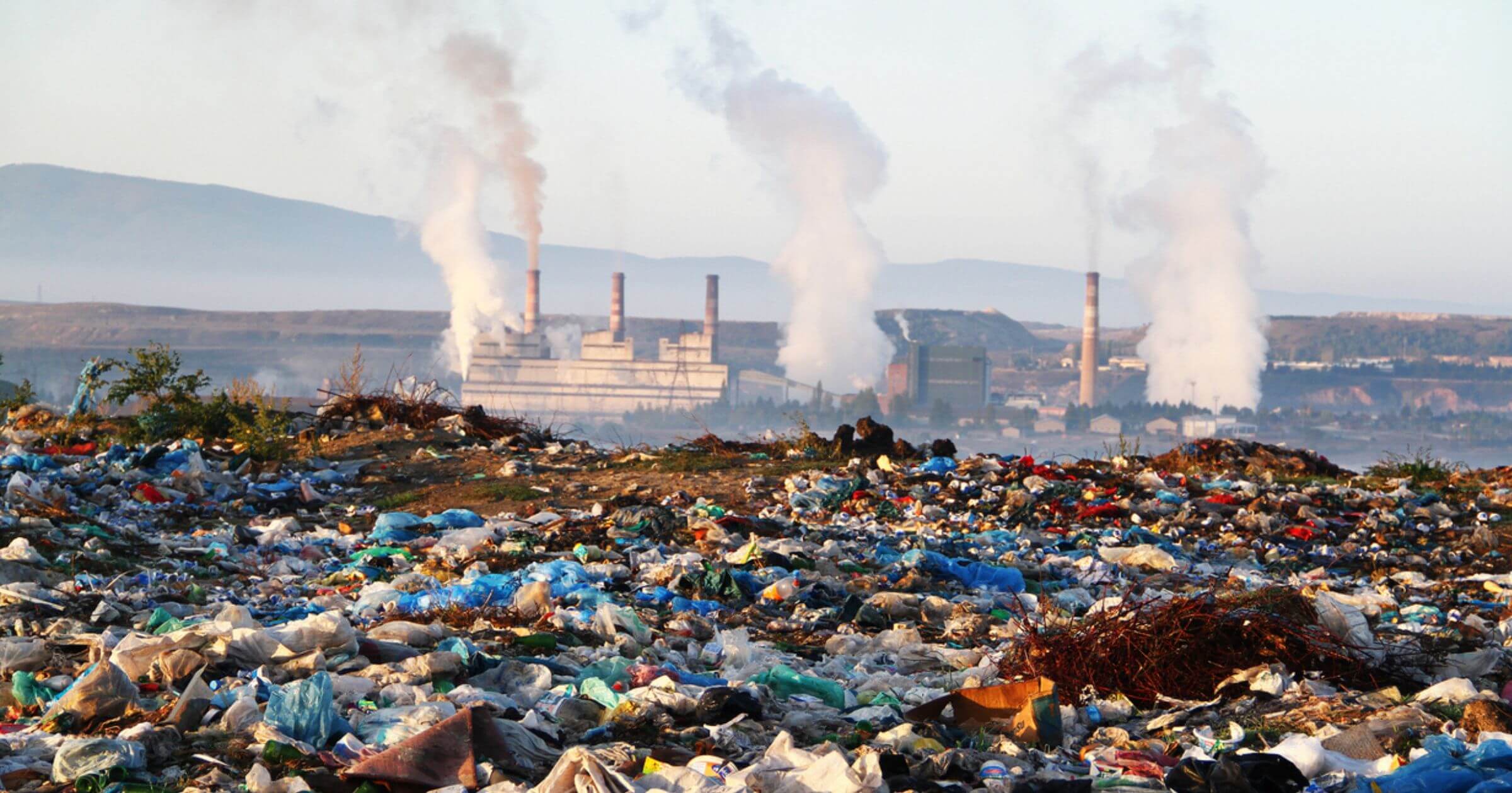 A view of plastic waste littered in open environment with factories polluting the atmosphere in the background