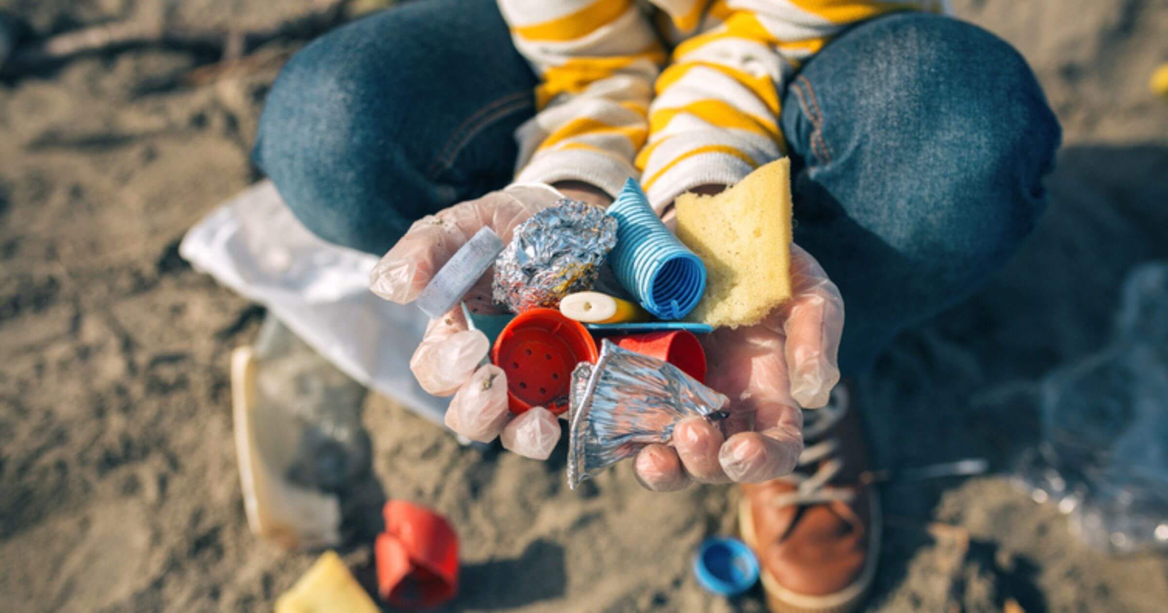 Person crouched down with two hands full of plastic items from a beach cleanup