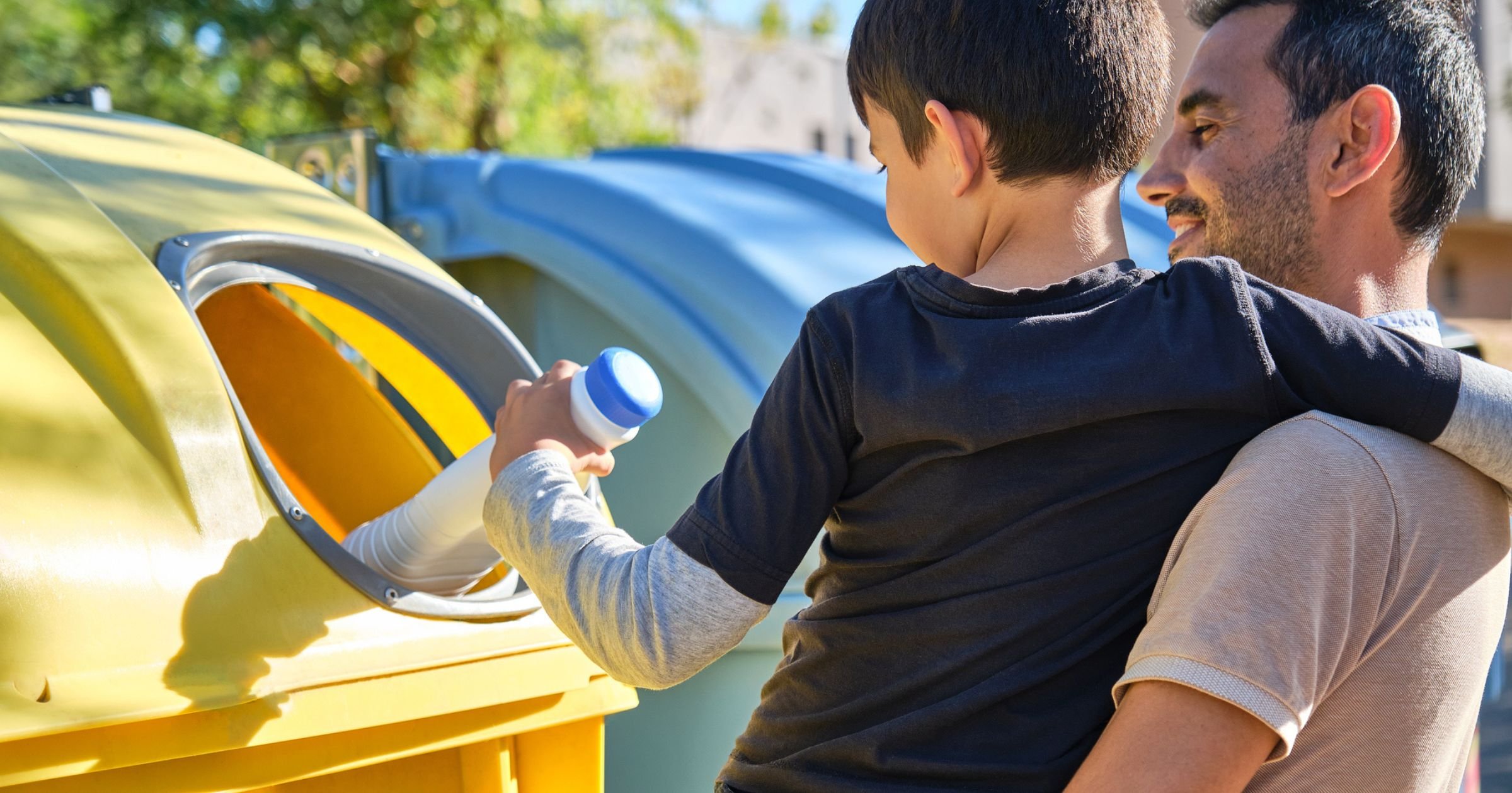 Father and son putting a plastic bottle in a yellow recycling bin