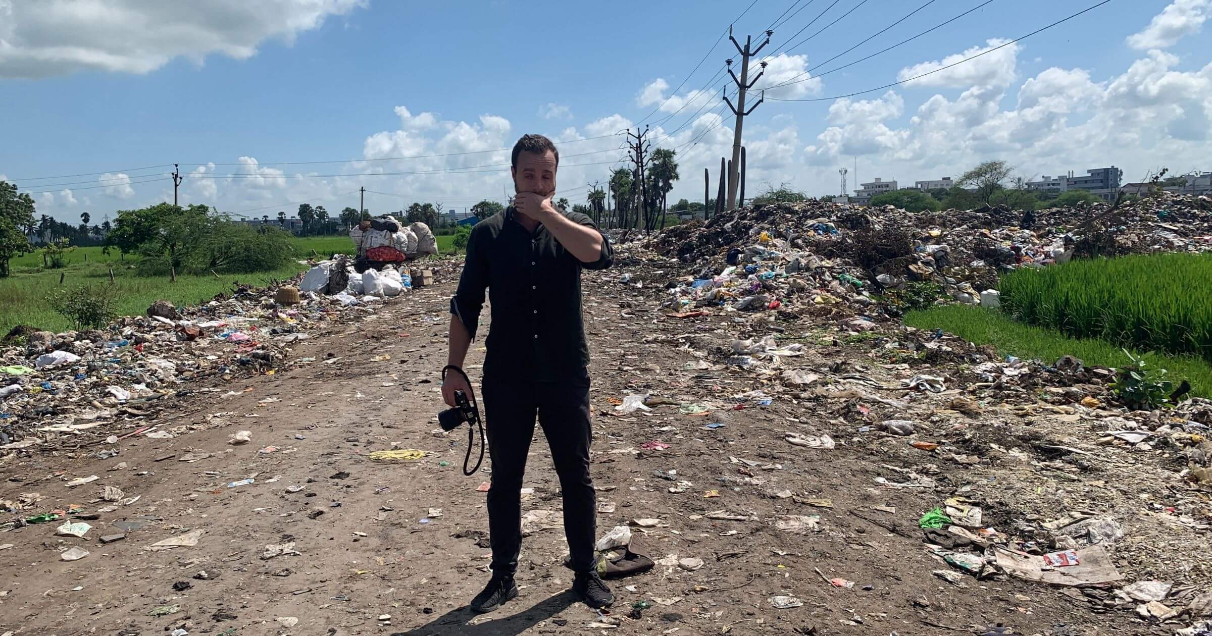 Joel Tasche, co-founder of CleanHub, stands in the middle of a muddy road with trash littered everywhere
