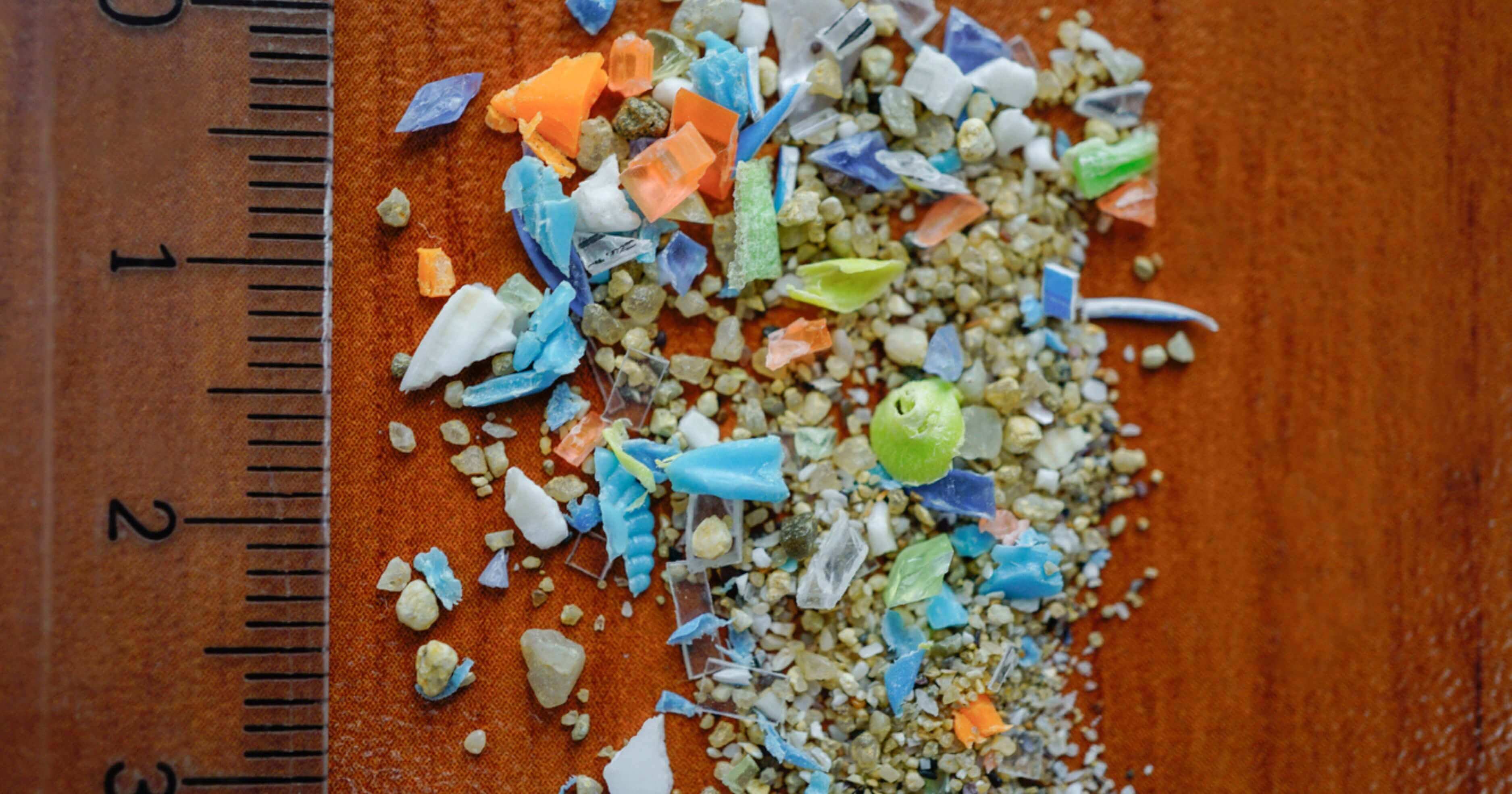 Lots of microplastics scattered on a table next to a ruler measuring them 