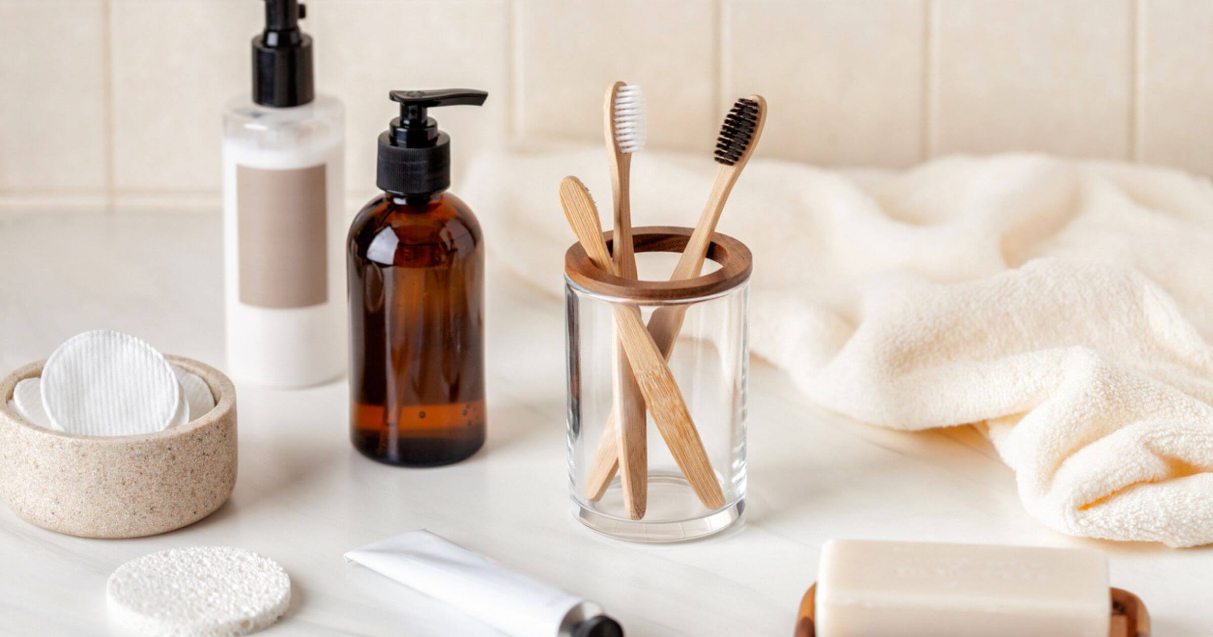 Plastic-free bathroom products with a neutral background including bamboo toothbrush cotton pads and glass bottles