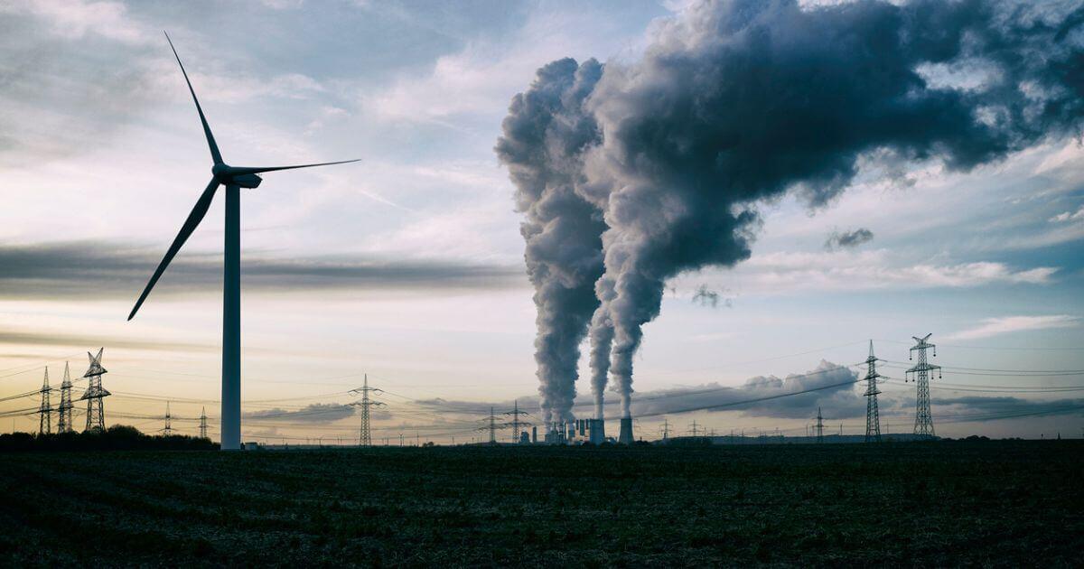 A silhouette of a wind turbine and fossil fuel fumes in the background