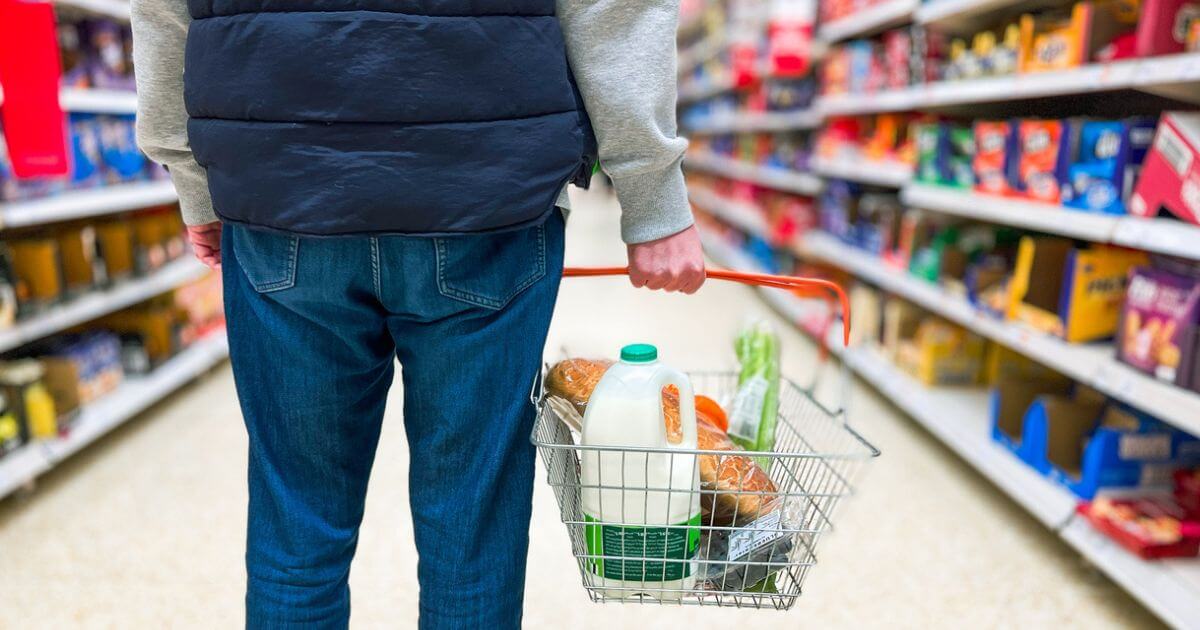 A view of someone holding a shopping basket in a supermarket from the waist down