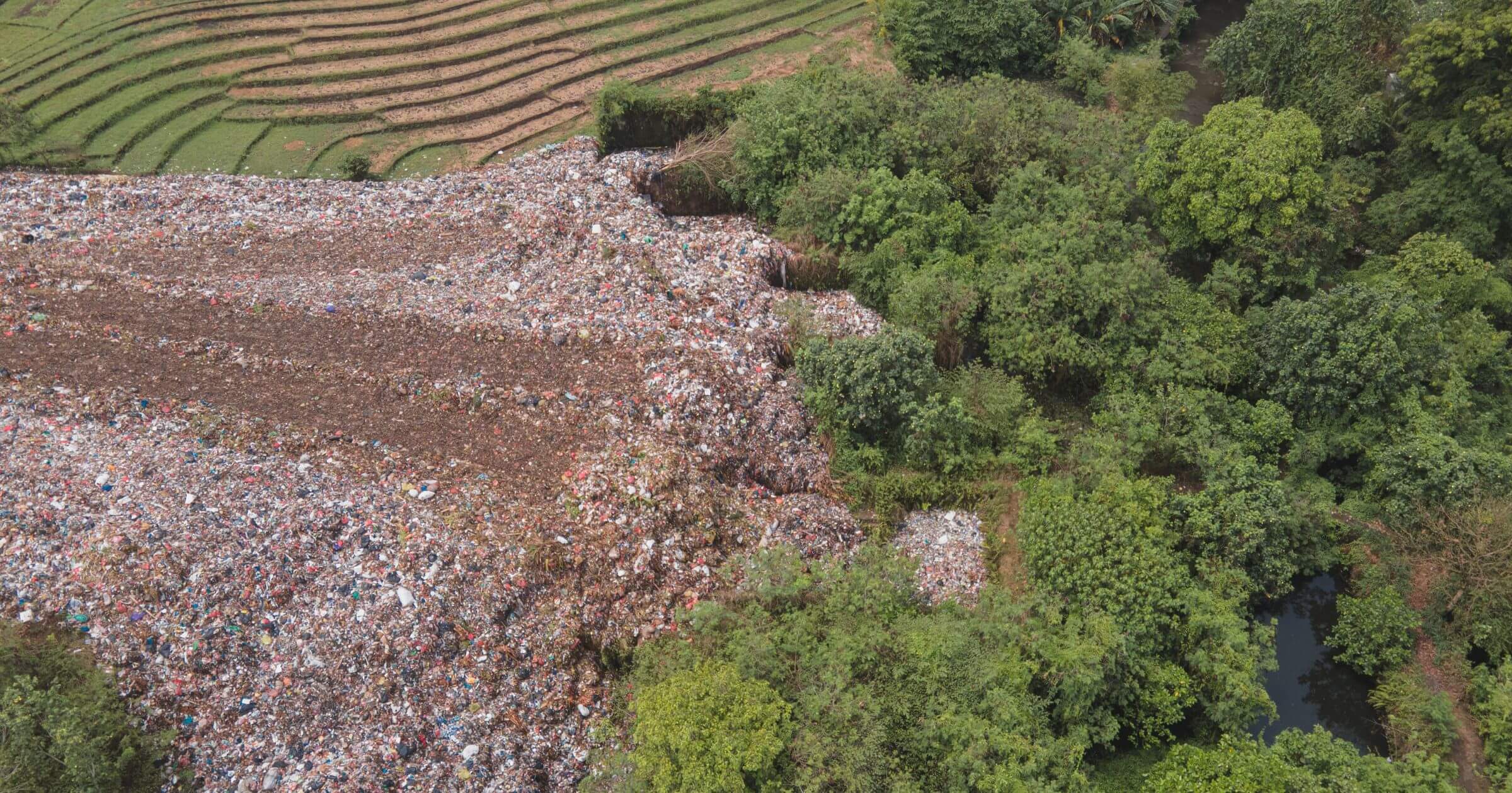 A bird's eye view of a landfill surrounded by padi fields and trees