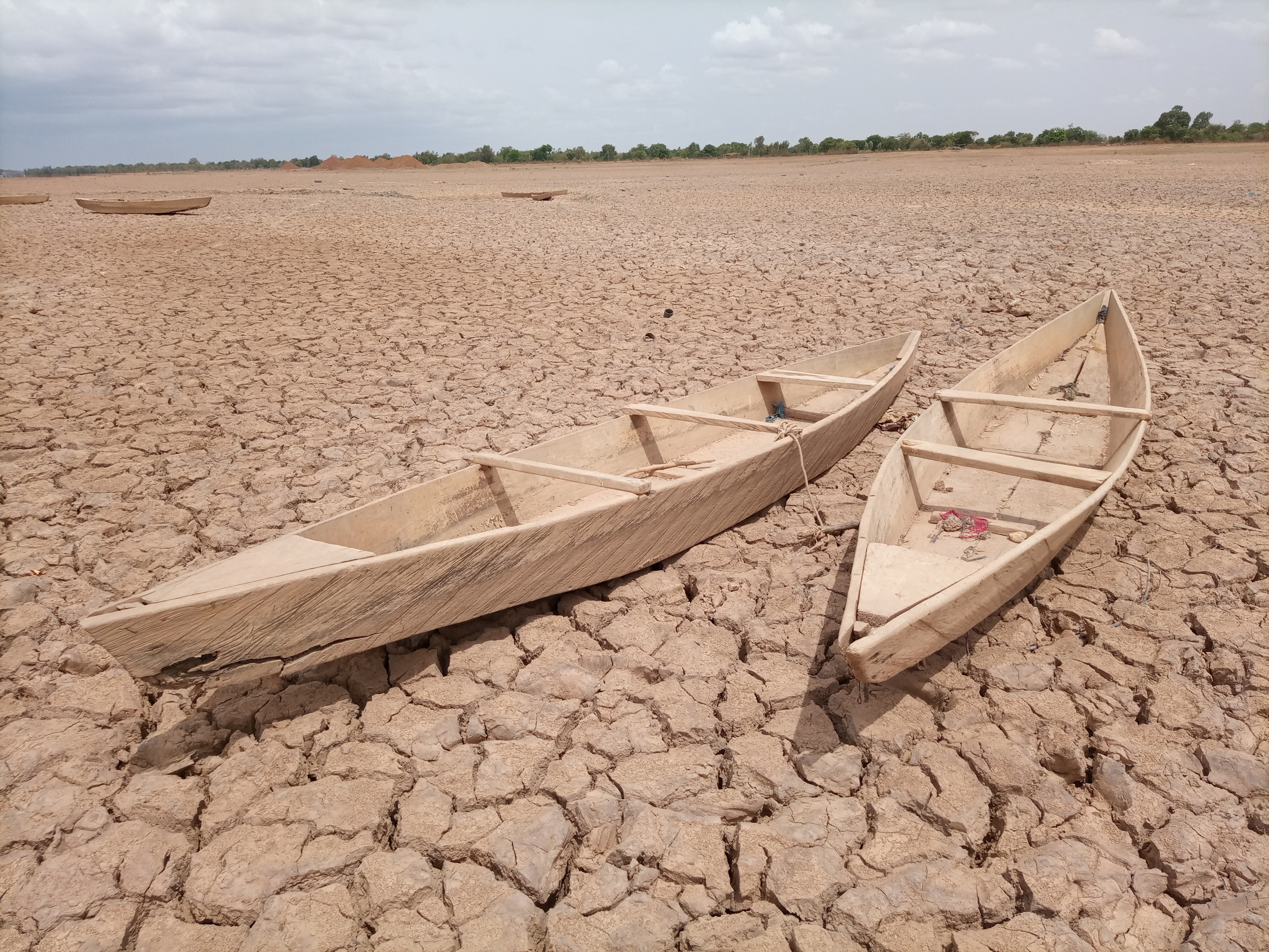 Image shows two wooden boats on an open landscape which is very dry and cracked 